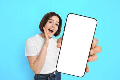 Happy woman showing mobile phone with blank screen on light blue background. Mockup for design