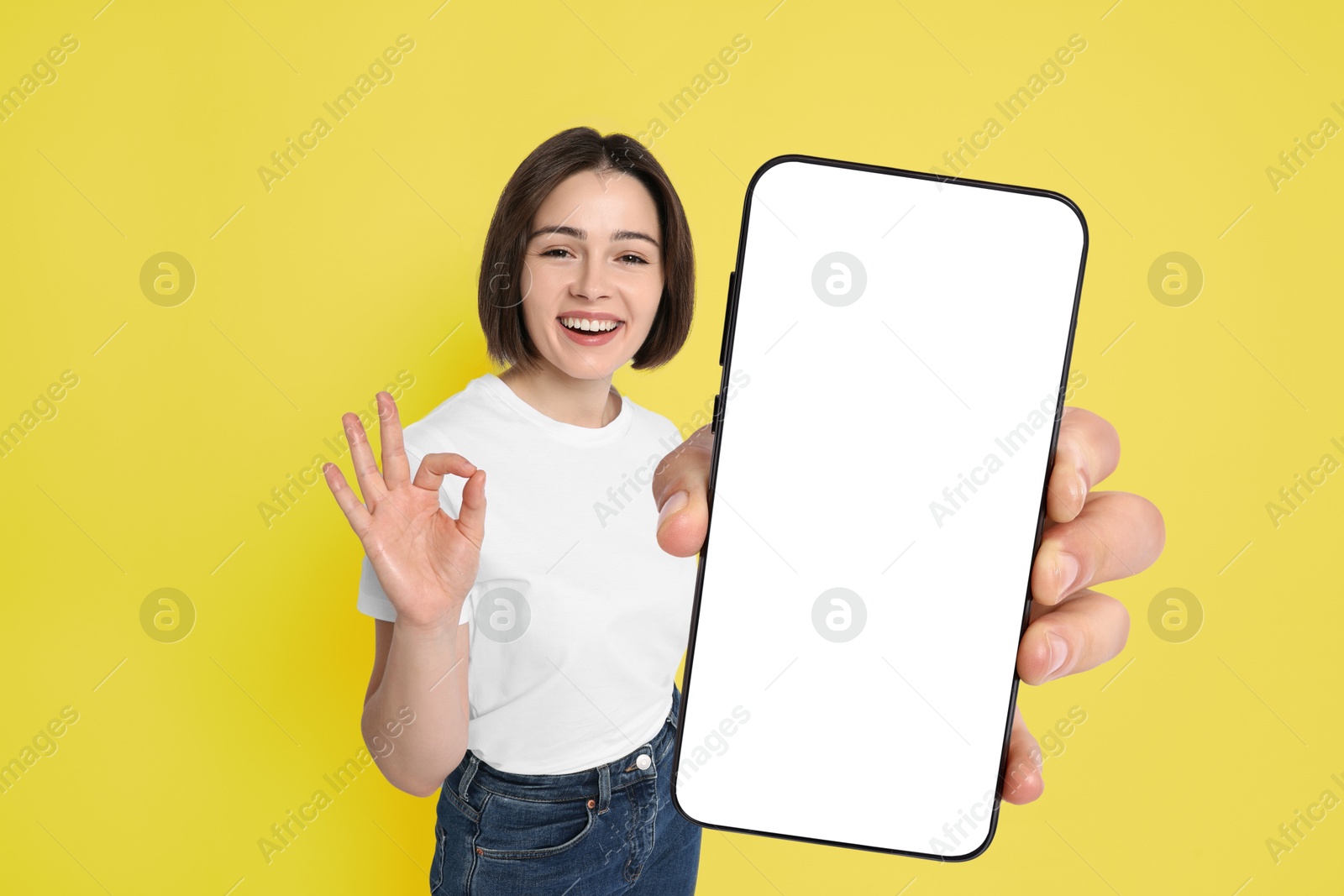 Image of Happy woman showing mobile phone with blank screen on yellow background. Mockup for design