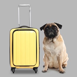 Image of Cute pug dog and yellow suitcase on grey background