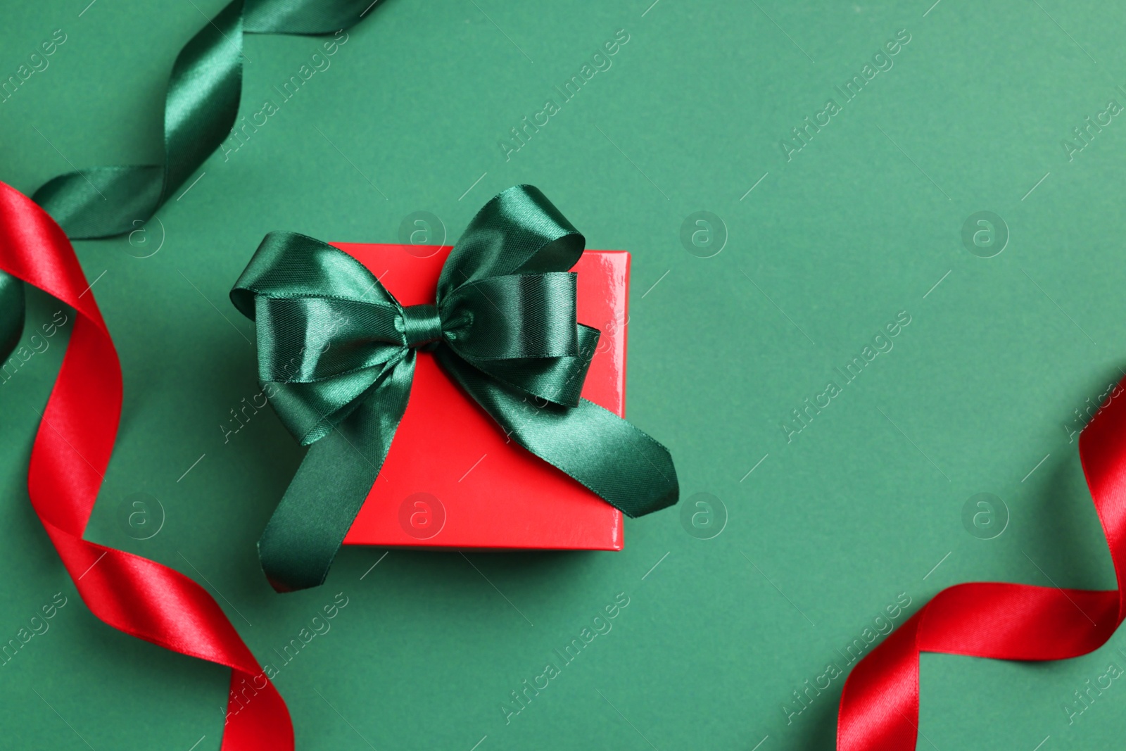 Photo of Beautiful red gift box with bright bow and ribbons on green background, flat lay. Space for text