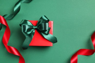 Photo of Beautiful red gift box with bright bow and ribbons on green background, flat lay. Space for text