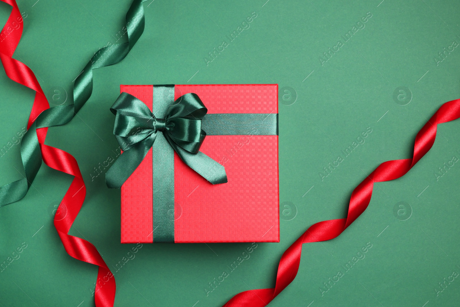 Photo of Beautiful red gift box with bright bow and ribbons on green background, flat lay