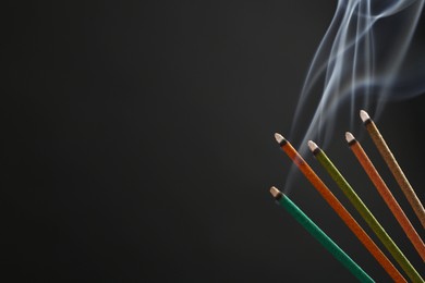 Photo of Aromatic incense sticks smoldering on black background. Space for text