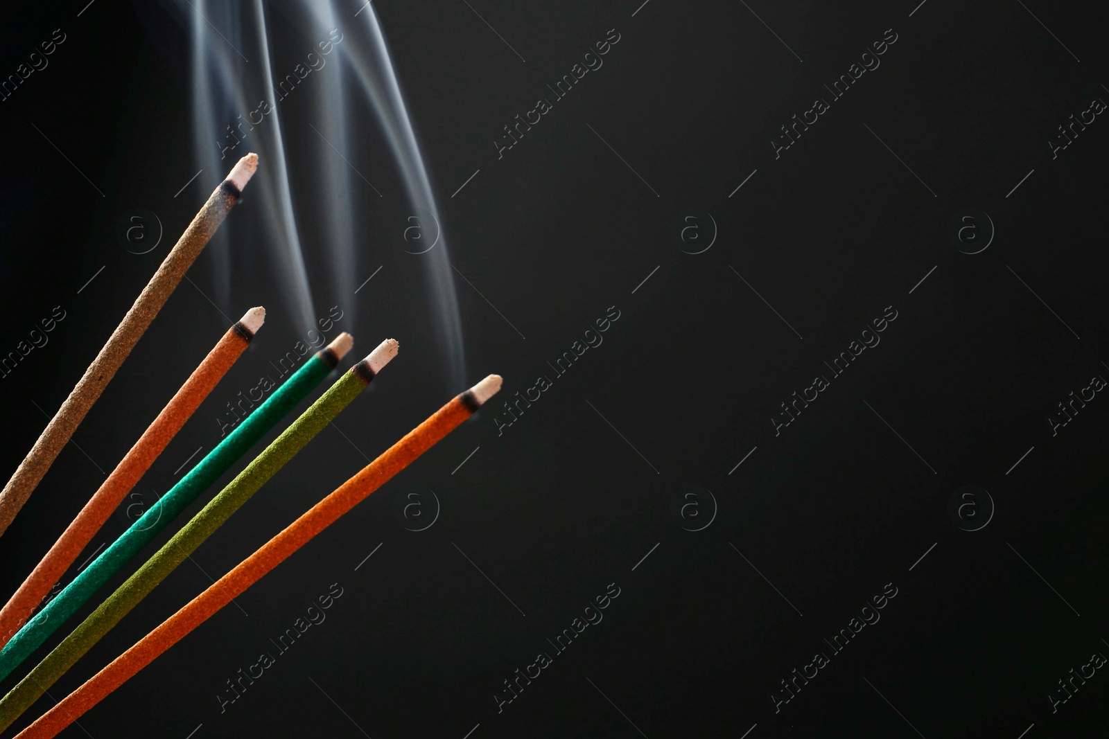 Photo of Aromatic incense sticks smoldering on black background. Space for text