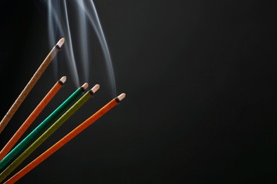 Photo of Aromatic incense sticks smoldering on black background. Space for text