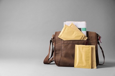 Photo of Brown postman's bag with envelopes and newspapers on grey background. Space for text