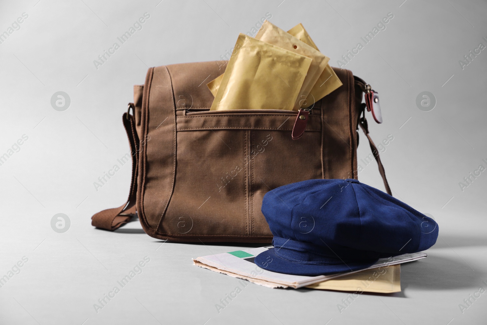 Photo of Brown postman's bag, envelopes, newspapers and hat on grey background