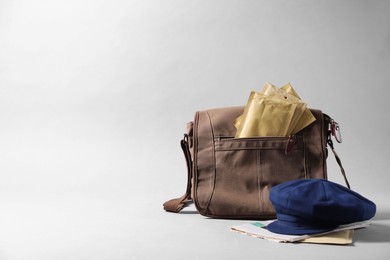 Photo of Brown postman's bag, envelopes, newspapers and hat on grey background. Space for text