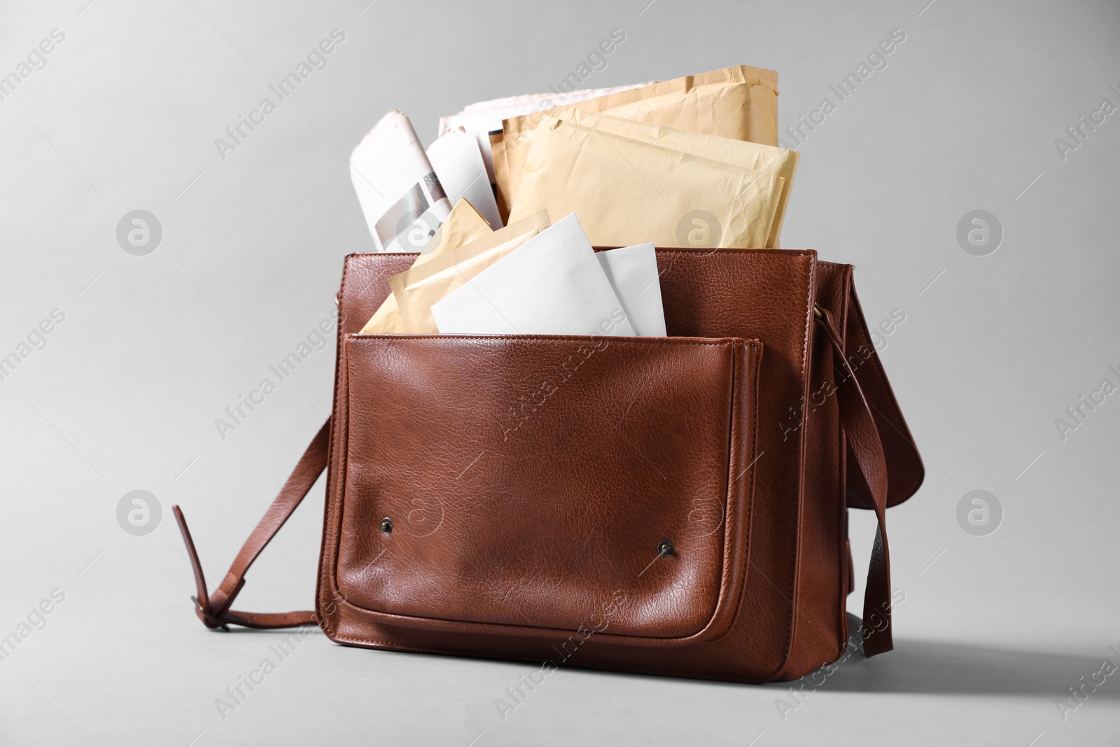 Photo of Brown postman's bag with envelopes and newspapers on grey background