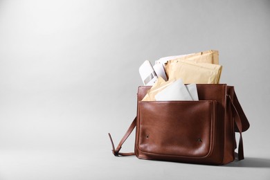 Photo of Brown postman's bag with envelopes and newspapers on grey background. Space for text