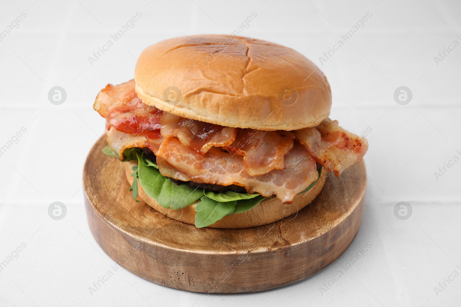 Photo of Delicious burger with bacon and greens on white table, closeup