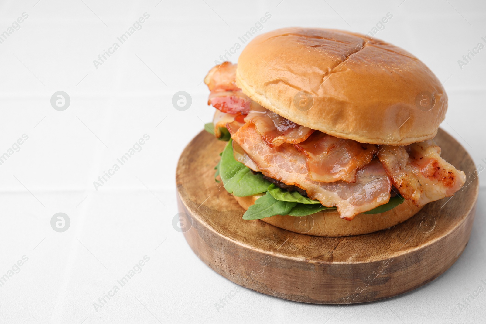 Photo of Delicious burger with bacon and greens on white table, closeup. Space for text