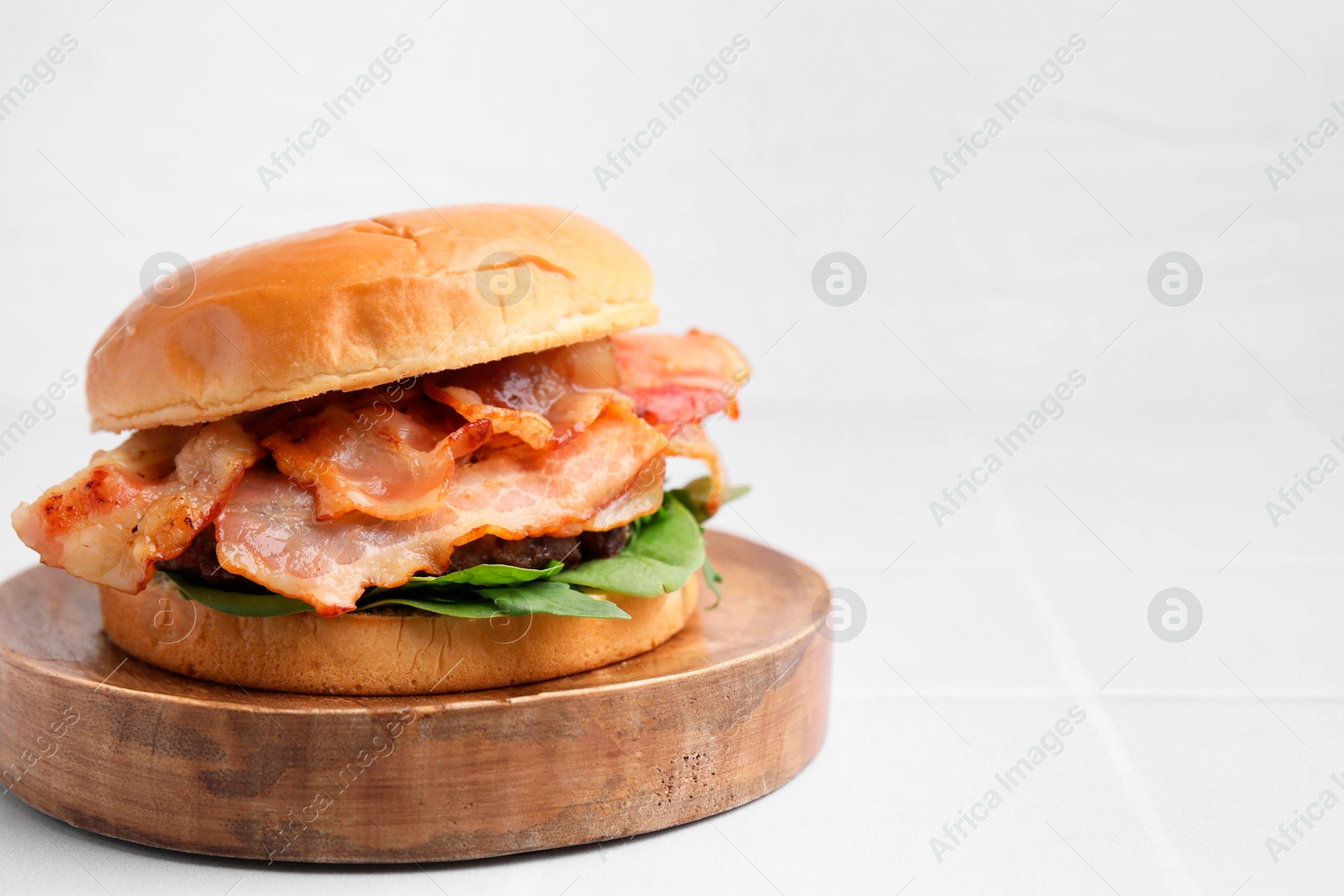 Photo of Delicious burger with bacon and greens on white table, closeup. Space for text