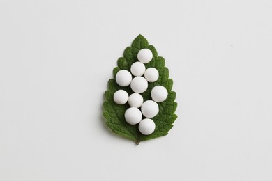 Homeopathic remedy. Many round pills and green leaf on white background, top view