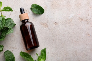 Photo of Bottle of essential oil and mint on light textured table, flat lay. Space for text