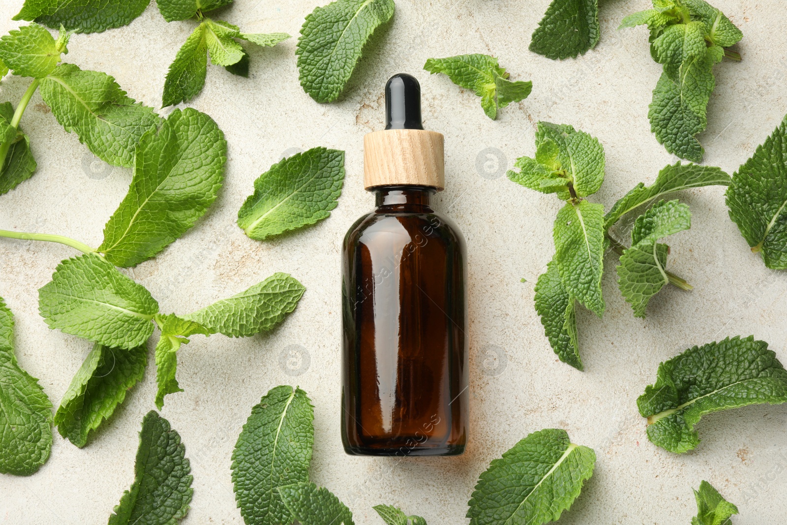 Photo of Bottle of essential oil and mint on light textured table, flat lay