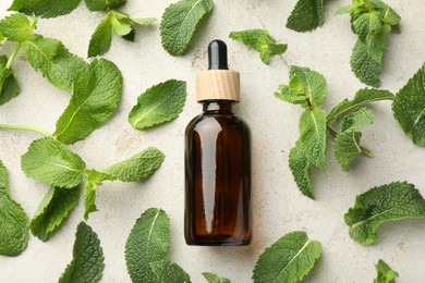 Photo of Bottle of essential oil and mint on light textured table, flat lay