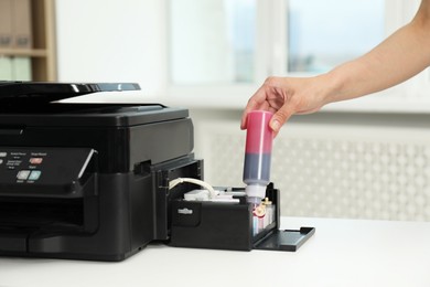 Photo of Woman refilling ink in modern printer at workplace indoors, closeup