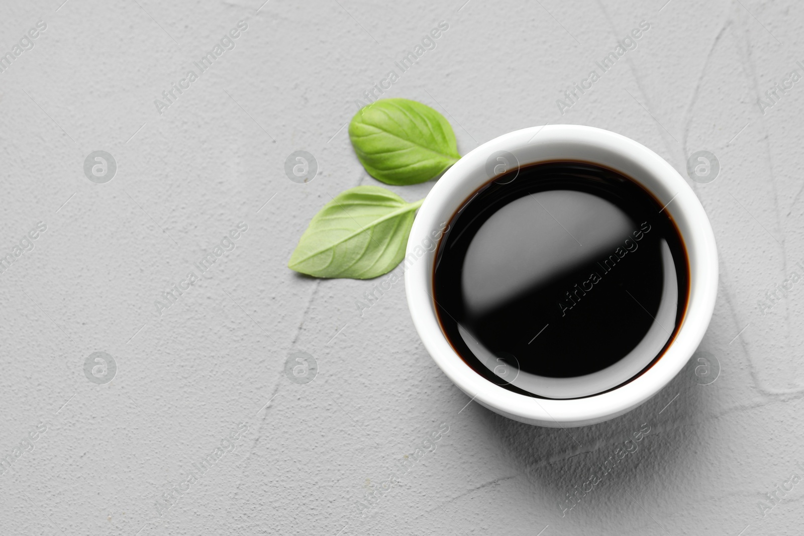 Photo of Balsamic vinegar and basil on light grey textured table, top view. Space for text