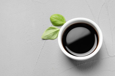 Photo of Balsamic vinegar and basil on light grey textured table, top view. Space for text