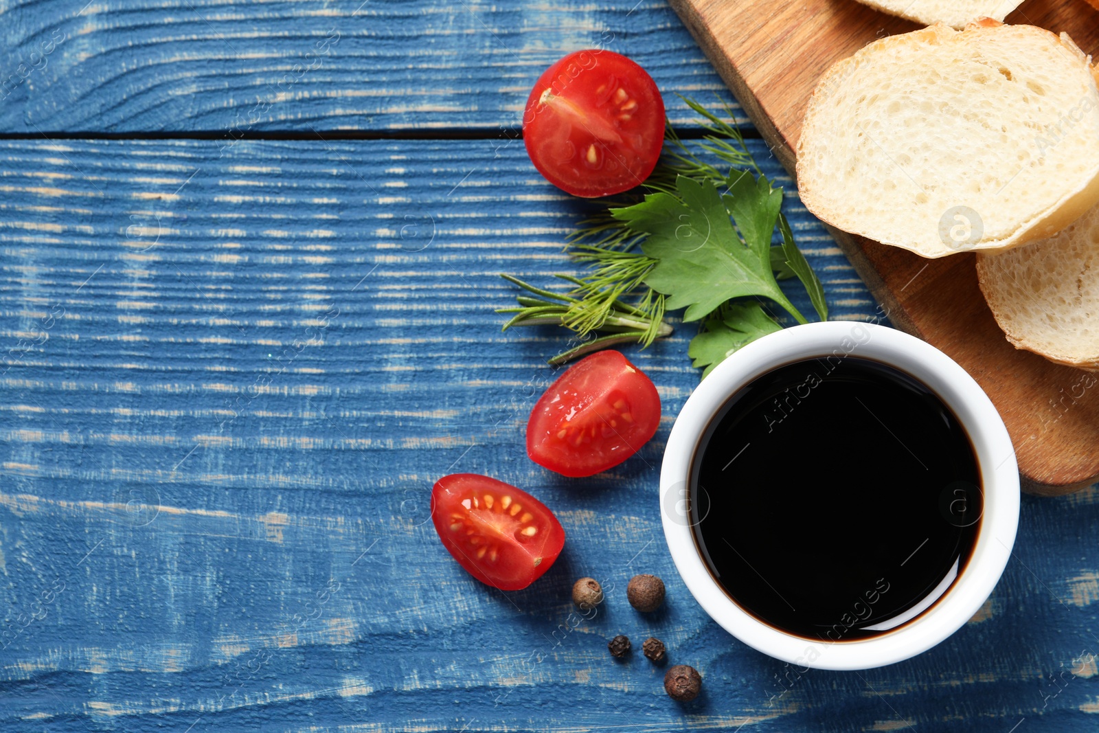 Photo of Balsamic vinegar, bread and other products on blue wooden table, flat lay. Space for text