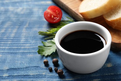 Photo of Balsamic vinegar, bread and other products on blue wooden table, closeup. Space for text