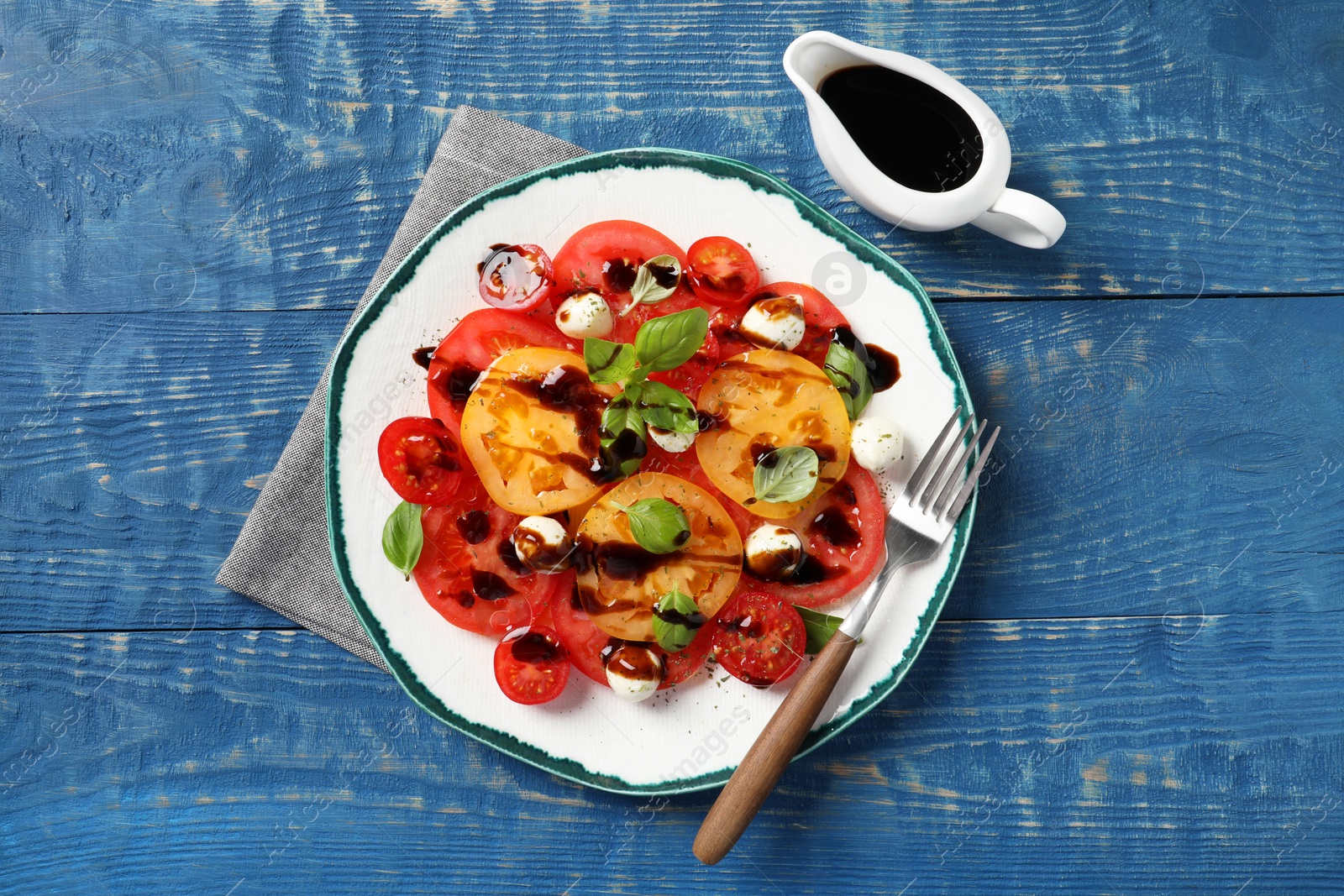 Photo of Tasty salad with balsamic vinegar, mozzarella and fork on blue wooden table, flat lay