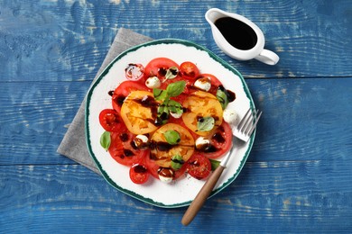 Photo of Tasty salad with balsamic vinegar, mozzarella and fork on blue wooden table, flat lay