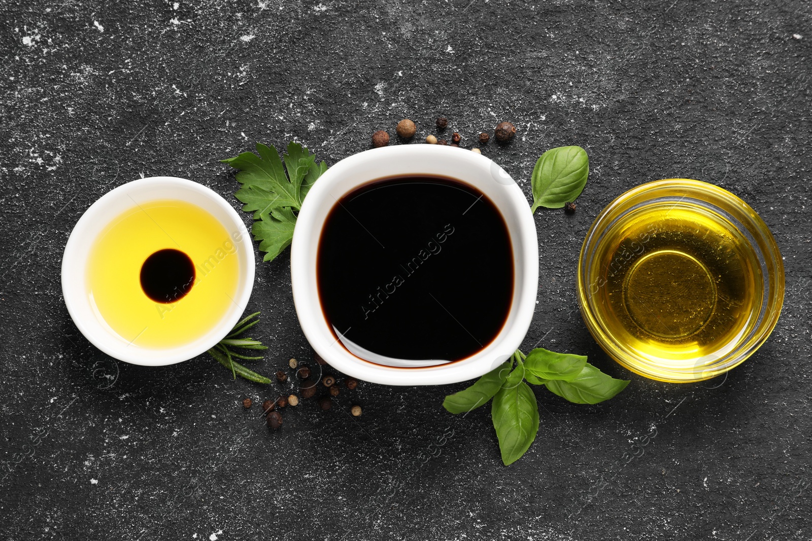 Photo of Balsamic vinegar, oil and other products on black textured table, flat lay