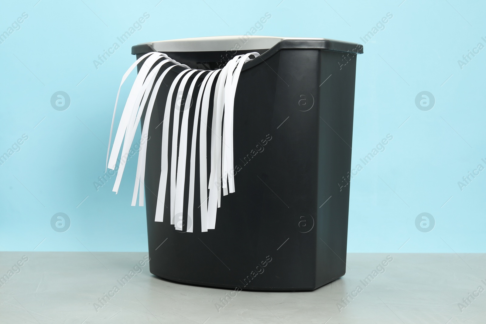 Photo of Shredder with paper strips on grey table against light blue background