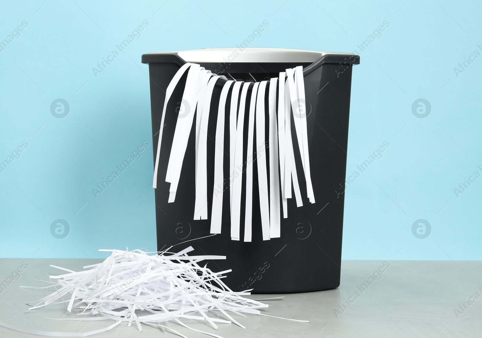 Photo of Shredder and paper strips on grey table against light blue background