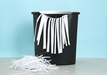 Photo of Shredder and paper strips on grey table against light blue background