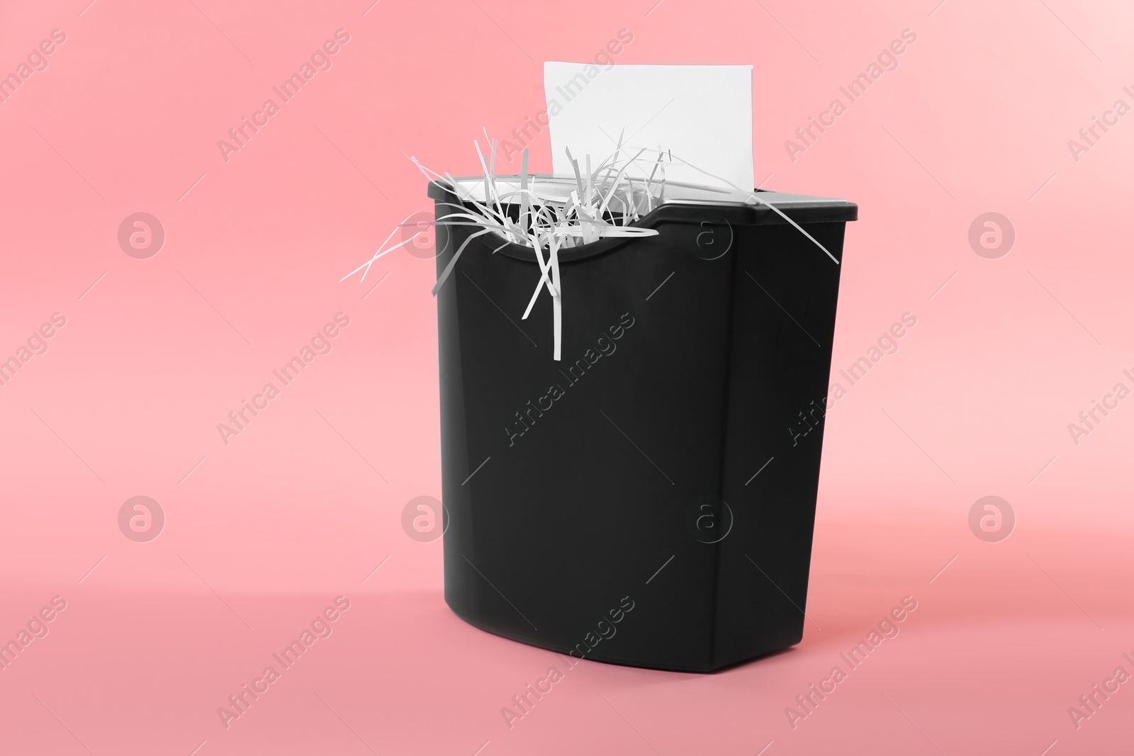 Photo of Destroying sheet of paper with shredder on pink background