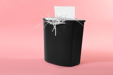 Destroying sheet of paper with shredder on pink background