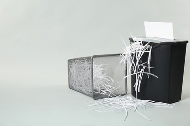 Photo of Shredder, metal basket and paper strips on light grey background, space for text