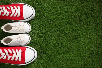 Photo of Big and small shoes on green grass, top view. Space for text