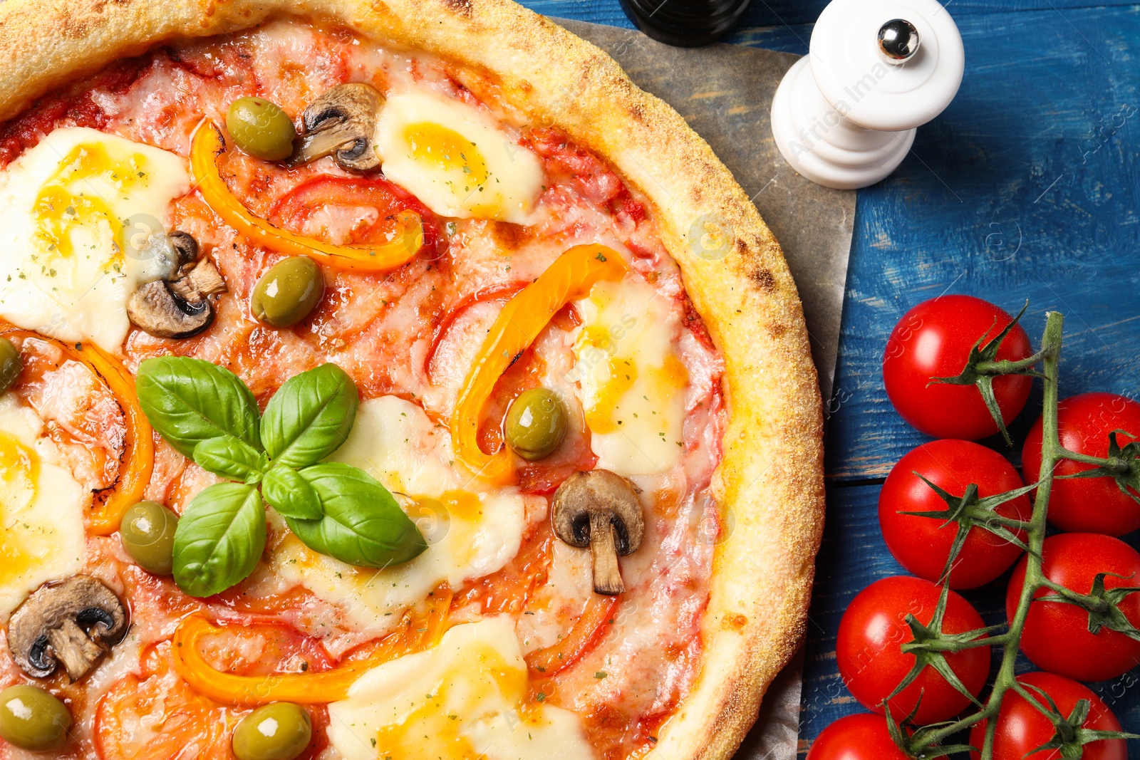 Photo of Delicious vegetarian pizza and ingredients on blue wooden table, top view