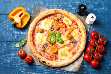 Photo of Delicious vegetarian pizza and ingredients on blue wooden table, top view