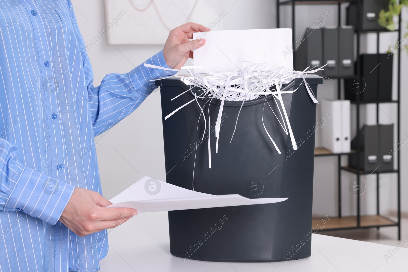 Photo of Woman destroying paper with shredder at white table in office, closeup