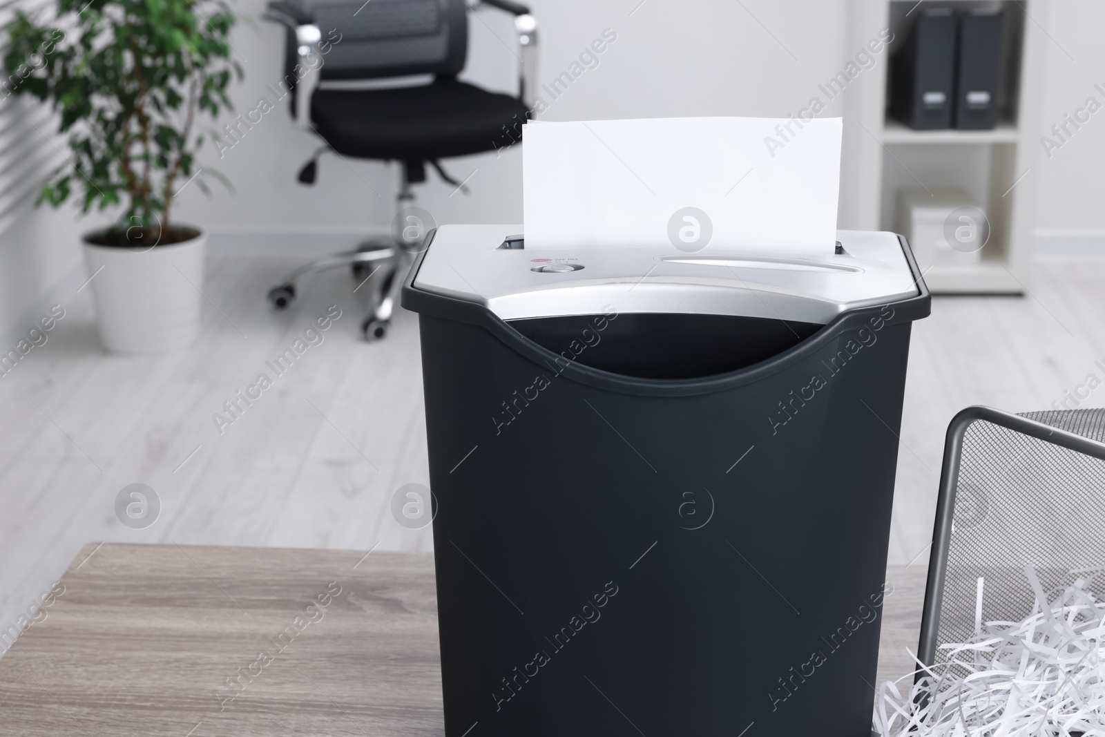 Photo of Destroying sheets of paper with shredder on wooden table in office