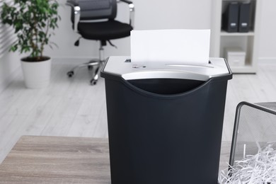 Photo of Destroying sheets of paper with shredder on wooden table in office