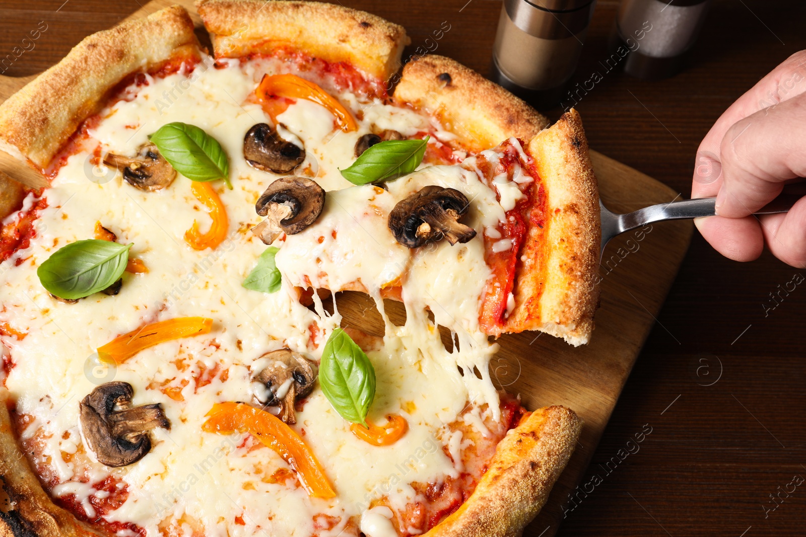 Photo of Man taking piece of delicious vegetarian pizza at wooden table, closeup