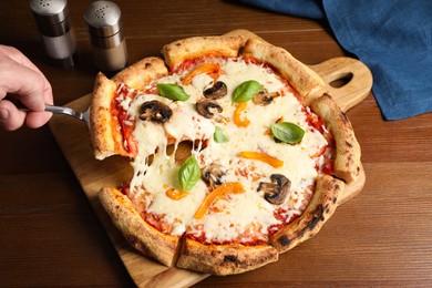 Photo of Man taking piece of delicious vegetarian pizza at wooden table, closeup