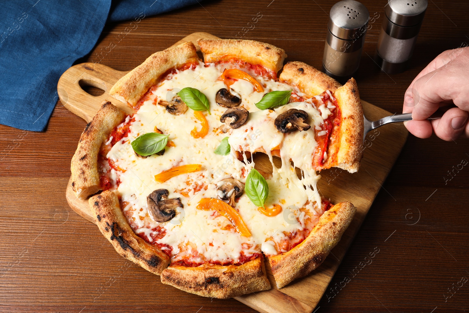 Photo of Man taking piece of delicious vegetarian pizza at wooden table, closeup