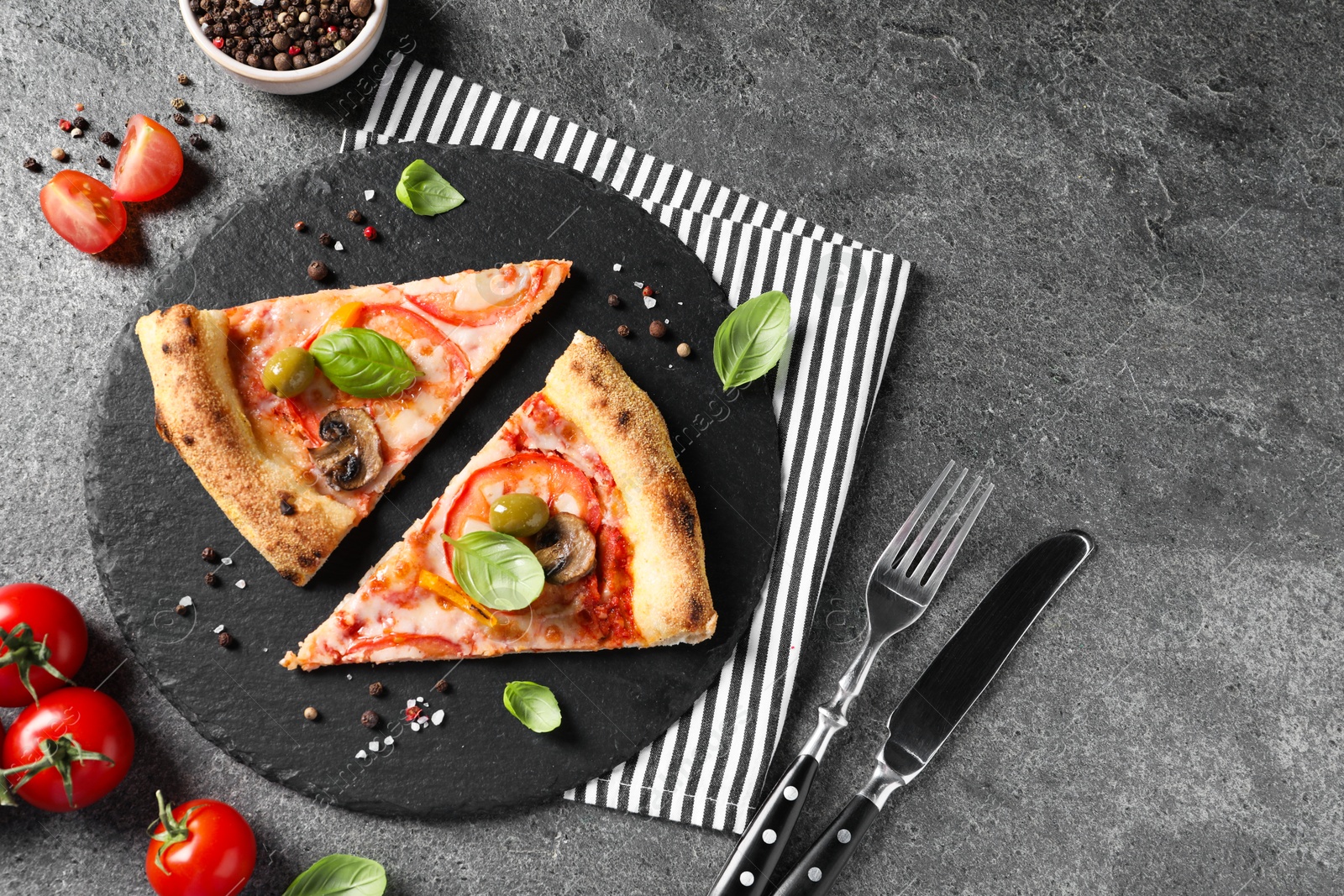 Photo of Cut delicious vegetarian pizza, cutlery and ingredients on grey table, top view. Space for text