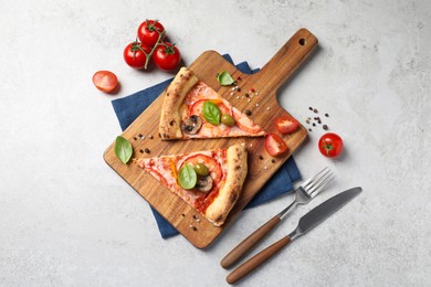 Photo of Cut delicious vegetarian pizza, cutlery and ingredients on light grey table, top view