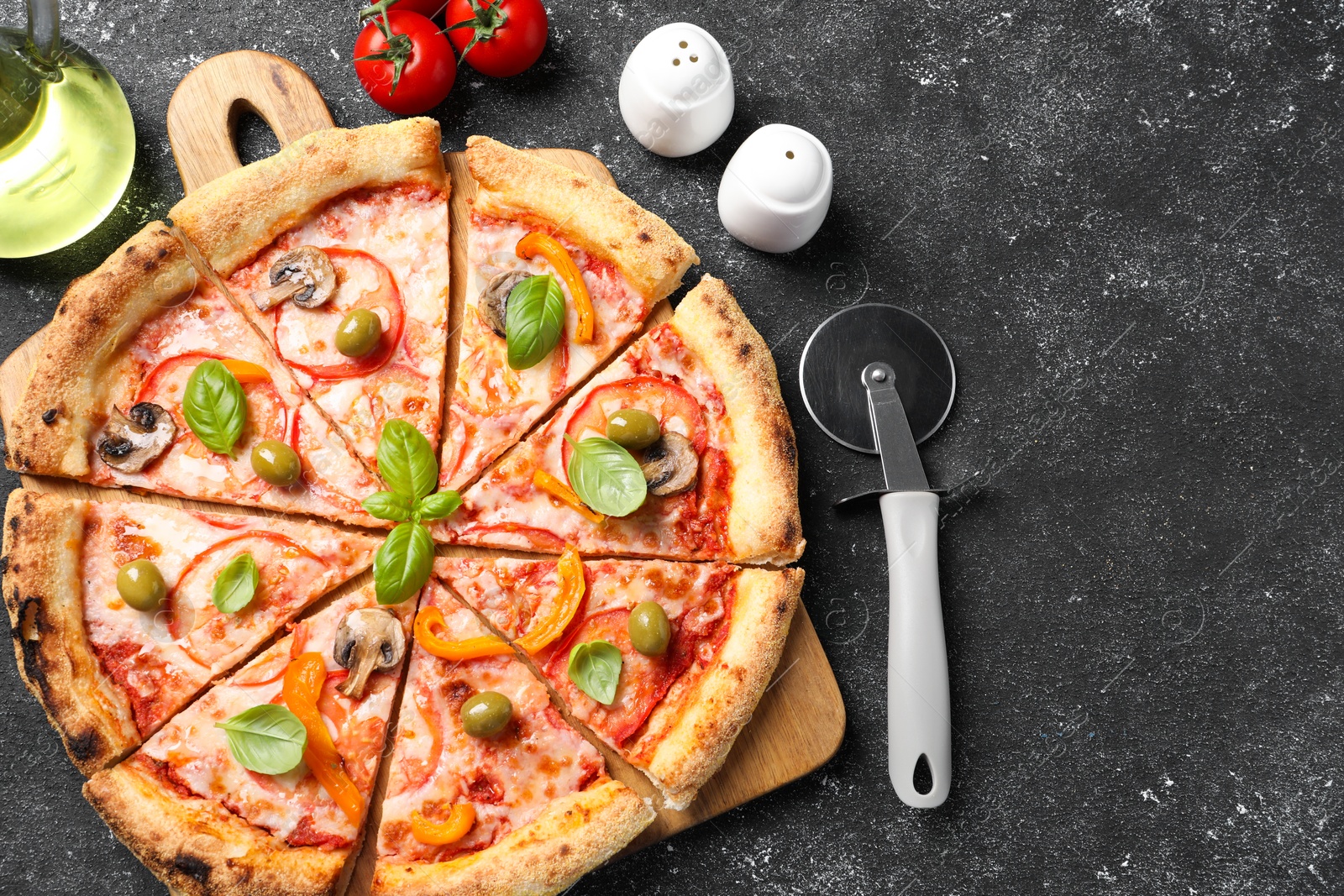 Photo of Cut delicious vegetarian pizza, cutter, oil and tomatoes on grey table, top view. Space for text