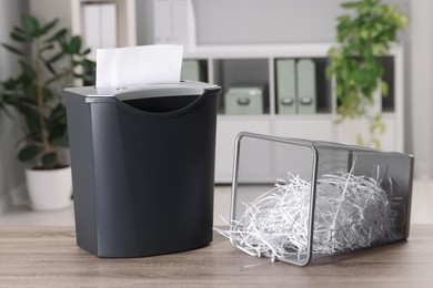 Photo of Destroying sheets with shredder and paper strips in metal bin on wooden table in office