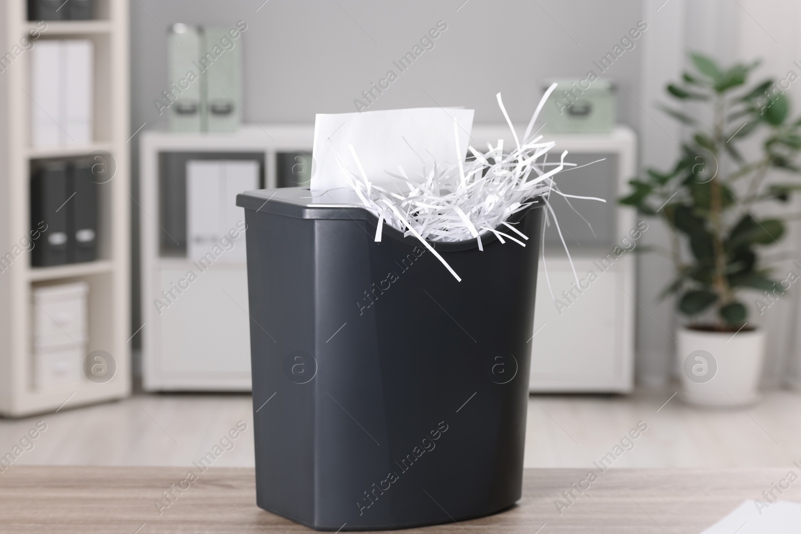 Photo of Destroying sheets of paper with shredder on wooden table in office