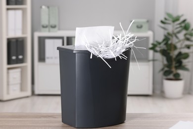 Photo of Destroying sheets of paper with shredder on wooden table in office